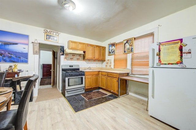 kitchen with stainless steel gas range, white fridge, tasteful backsplash, sink, and light hardwood / wood-style flooring