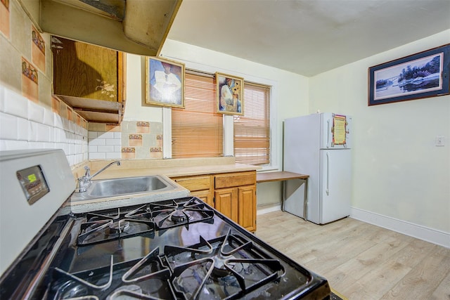 kitchen featuring decorative backsplash, sink, light hardwood / wood-style flooring, range with gas stovetop, and white refrigerator