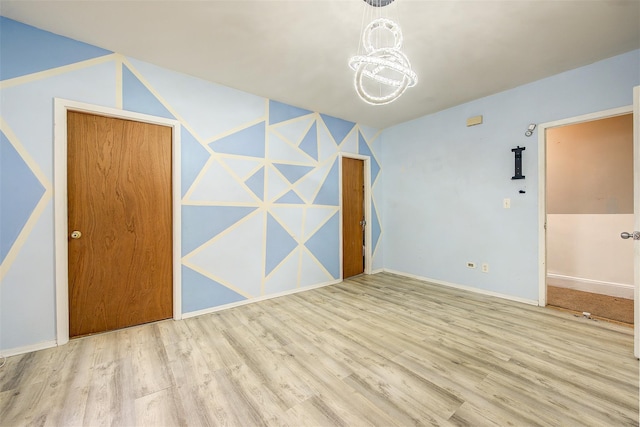 empty room with light wood-type flooring and an inviting chandelier