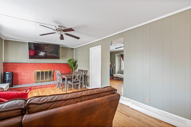 living room featuring ceiling fan, ornamental molding, a brick fireplace, a baseboard radiator, and light wood-type flooring