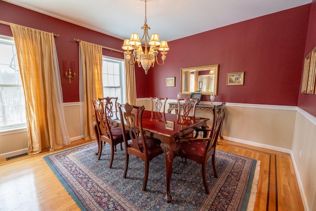 dining room featuring a chandelier, a wainscoted wall, visible vents, and wood finished floors