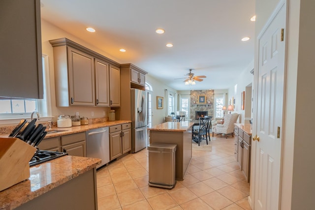 kitchen featuring ceiling fan, light tile patterned floors, light stone counters, appliances with stainless steel finishes, and a fireplace