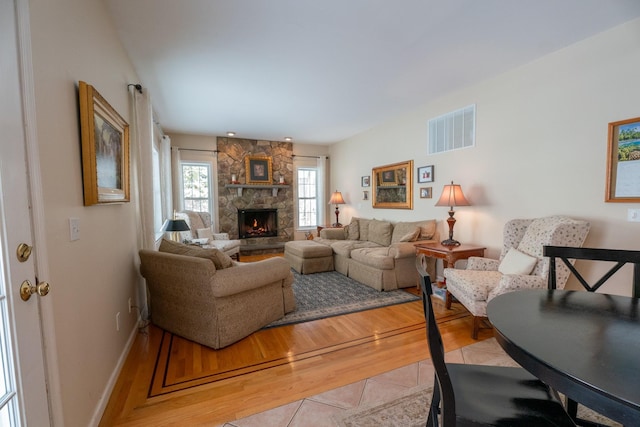 living area featuring visible vents, a stone fireplace, light wood-type flooring, and baseboards