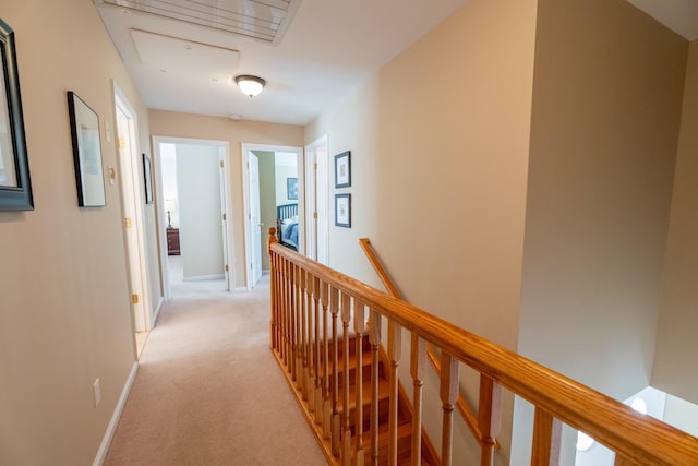 hall with an upstairs landing, attic access, light carpet, and baseboards