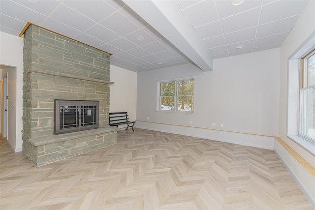 unfurnished living room with a paneled ceiling, a stone fireplace, and light parquet floors