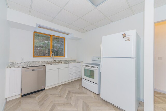 kitchen with white appliances, white cabinets, a paneled ceiling, sink, and light stone counters