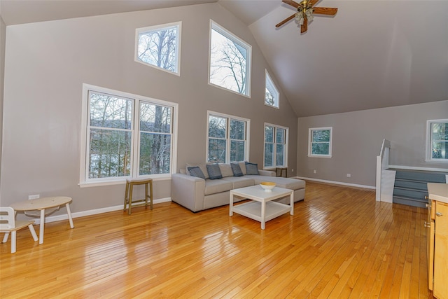 living room with light wood-type flooring, ceiling fan, a wealth of natural light, and a towering ceiling