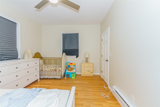 bedroom featuring ceiling fan, a baseboard heating unit, and light hardwood / wood-style flooring