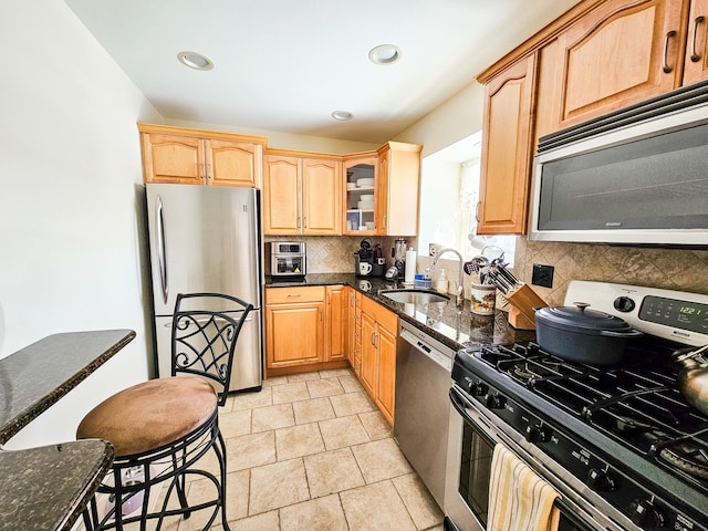 kitchen with dark stone countertops, decorative backsplash, a kitchen bar, sink, and appliances with stainless steel finishes