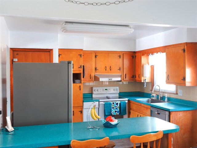 kitchen with under cabinet range hood, brown cabinets, tasteful backsplash, a sink, and stainless steel appliances