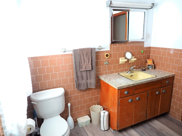 bathroom featuring tile walls, wainscoting, wood finished floors, vanity, and toilet
