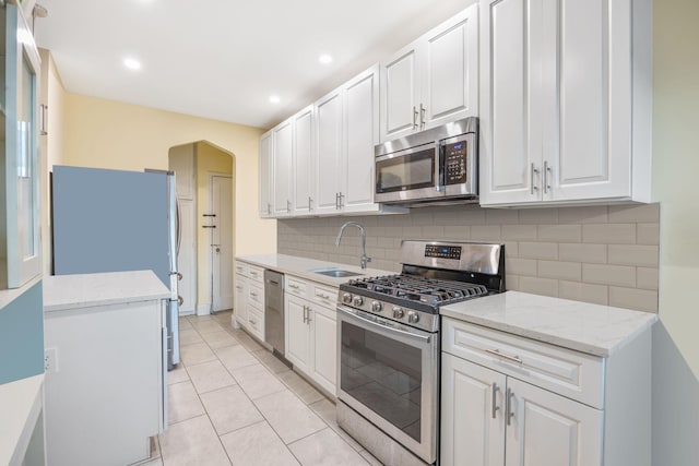 kitchen with sink, appliances with stainless steel finishes, white cabinetry, backsplash, and light stone countertops