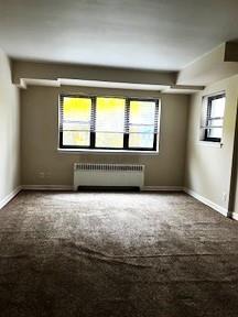 spare room with baseboards, carpet flooring, and radiator