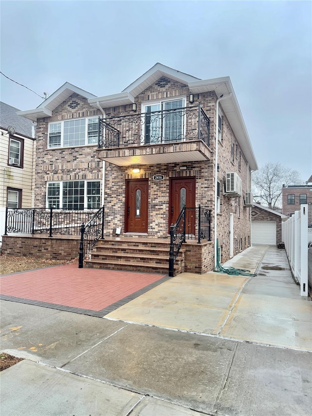 view of front of home featuring a garage, a balcony, an outdoor structure, and a wall mounted air conditioner