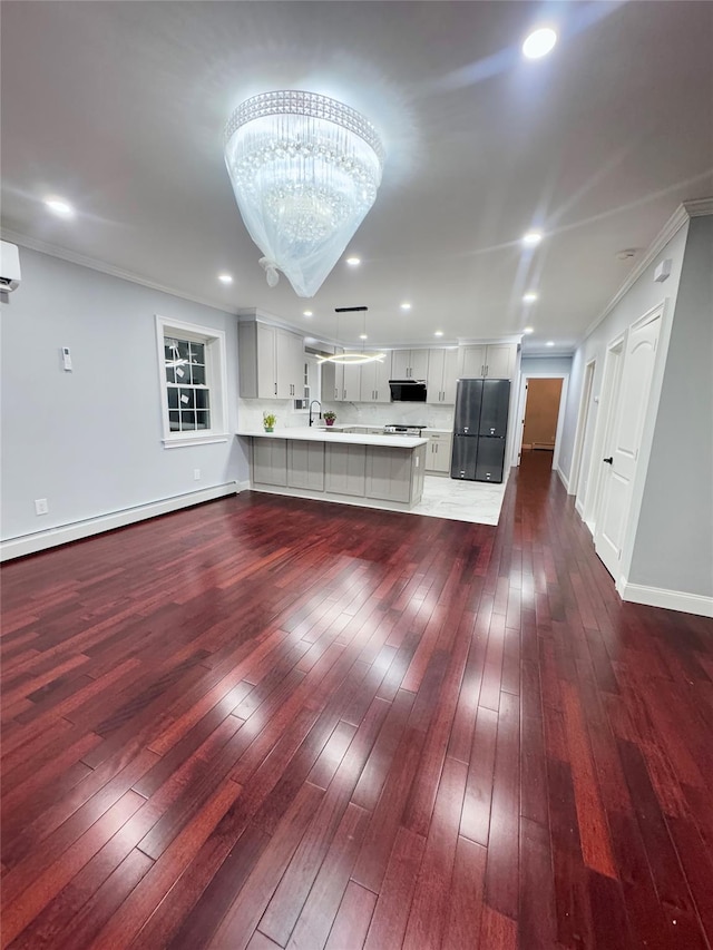 unfurnished living room with a baseboard radiator, hardwood / wood-style floors, crown molding, and a chandelier