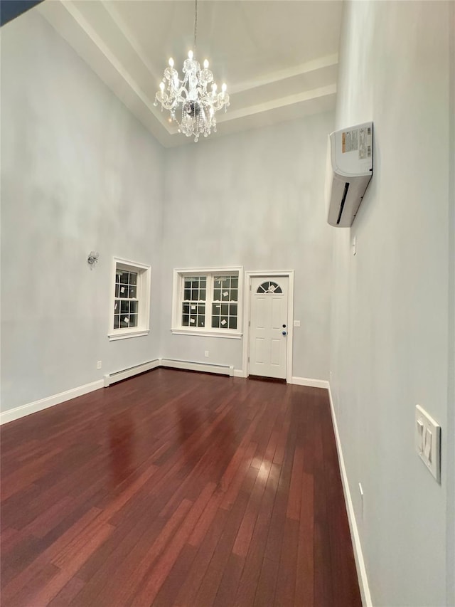 interior space with an inviting chandelier, a high ceiling, a wall mounted air conditioner, baseboard heating, and wood-type flooring