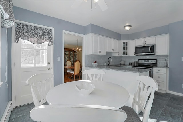 kitchen with sink, a baseboard radiator, appliances with stainless steel finishes, white cabinets, and decorative backsplash