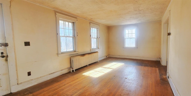 empty room with hardwood / wood-style floors, radiator heating unit, and a textured ceiling