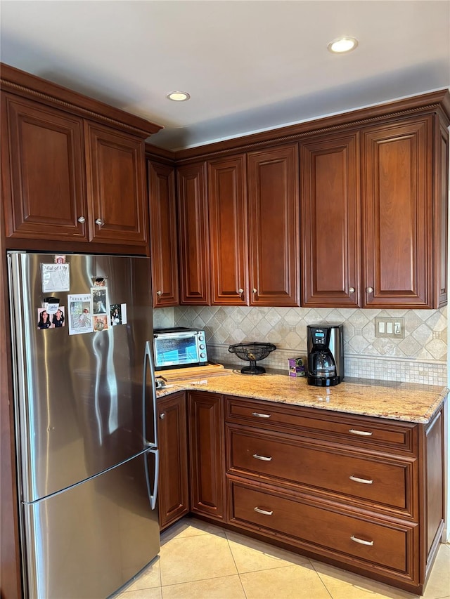 kitchen featuring light tile patterned flooring, light stone counters, backsplash, and stainless steel refrigerator