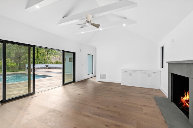 unfurnished living room with beam ceiling, ceiling fan, hardwood / wood-style flooring, and high vaulted ceiling