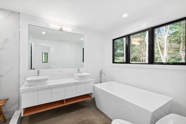 bathroom featuring a bath, concrete flooring, a wealth of natural light, and vanity