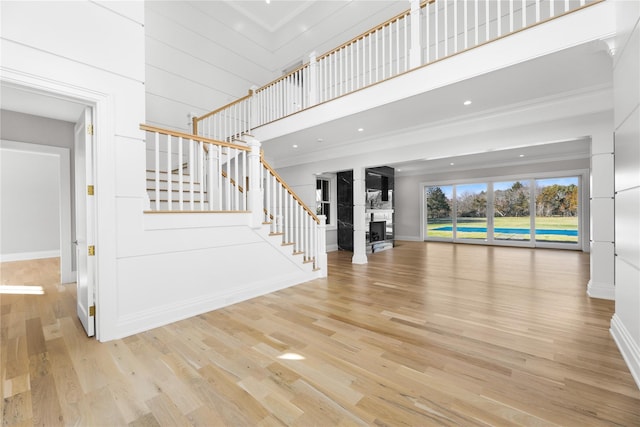 unfurnished living room with ornamental molding, light hardwood / wood-style floors, and a high ceiling