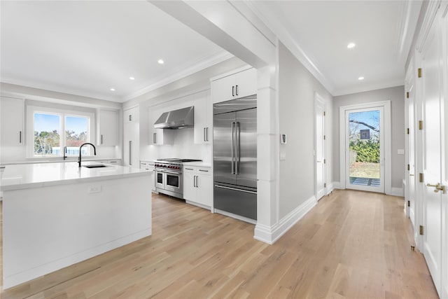 kitchen featuring white cabinetry, high end appliances, crown molding, wall chimney range hood, and light hardwood / wood-style flooring