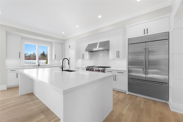 kitchen featuring sink, stainless steel built in refrigerator, an island with sink, white cabinets, and wall chimney exhaust hood