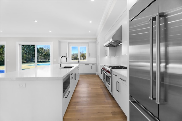 kitchen featuring wall chimney range hood, sink, a kitchen island with sink, white cabinetry, and high quality appliances