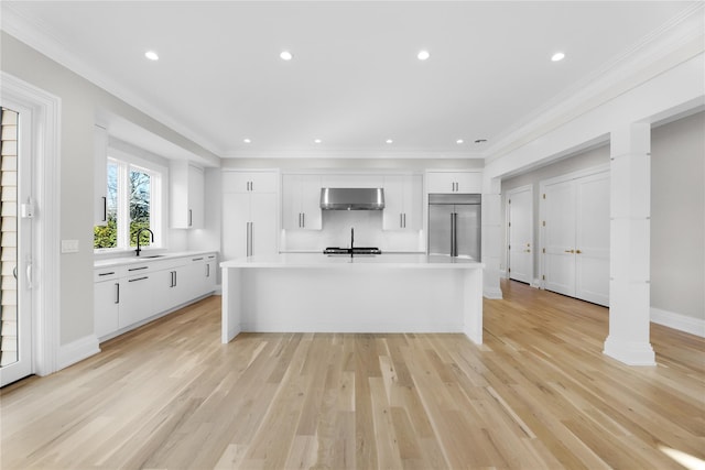 kitchen featuring built in refrigerator, an island with sink, white cabinets, and crown molding