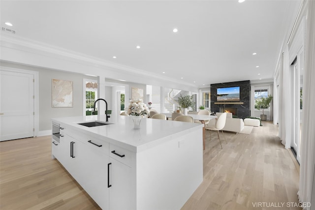 kitchen featuring sink, a center island with sink, ornamental molding, light hardwood / wood-style floors, and white cabinets