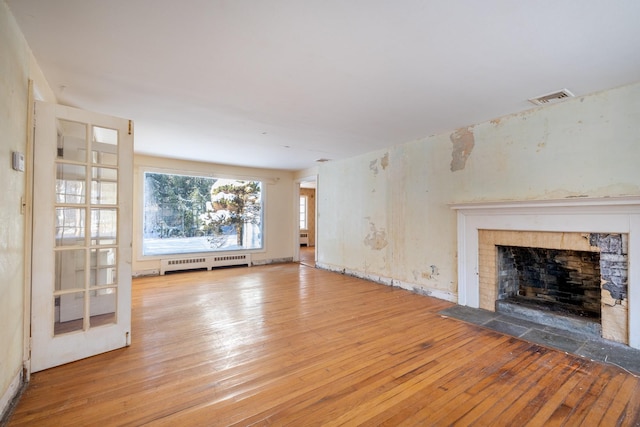 unfurnished living room with a tiled fireplace, wood-type flooring, and baseboard heating