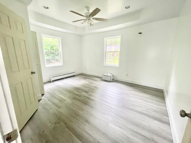 empty room featuring a baseboard radiator, ceiling fan, light hardwood / wood-style floors, and a tray ceiling