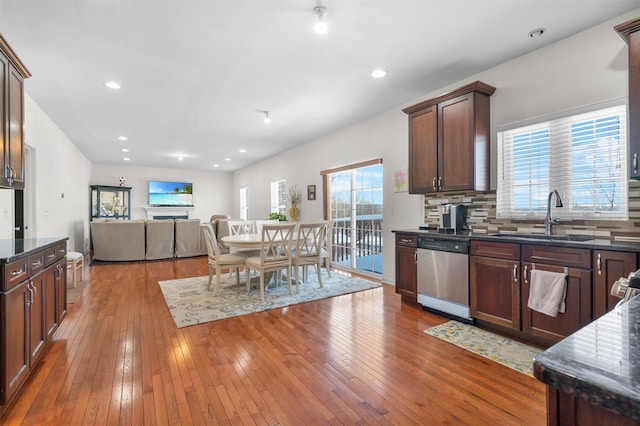 kitchen featuring hardwood / wood-style floors, dark stone counters, decorative backsplash, sink, and stainless steel dishwasher