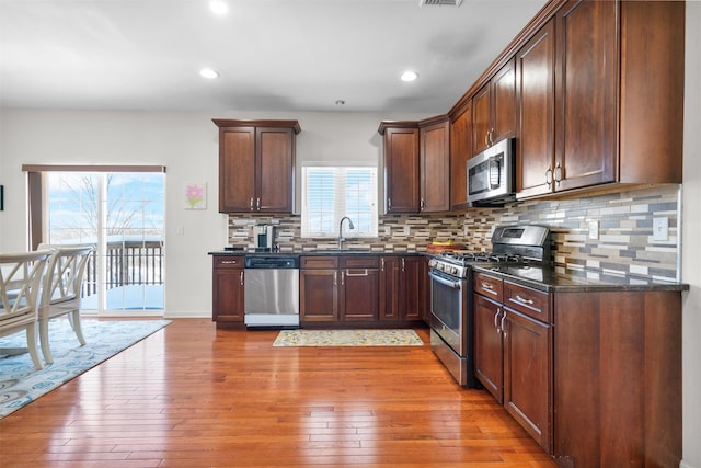 kitchen with appliances with stainless steel finishes, dark stone counters, decorative backsplash, sink, and light hardwood / wood-style flooring