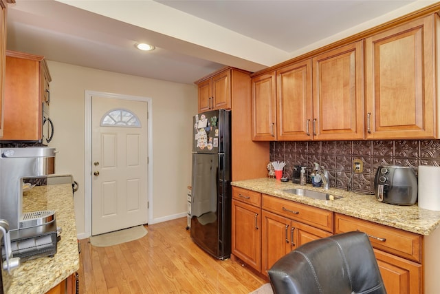 kitchen with sink, light stone counters, black refrigerator, light hardwood / wood-style floors, and backsplash