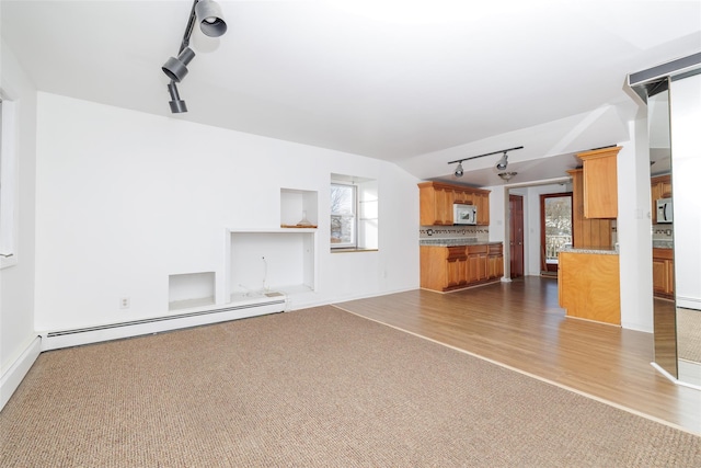 unfurnished living room with baseboard heating, lofted ceiling, carpet flooring, and rail lighting