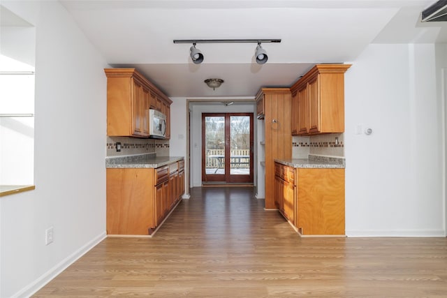 kitchen with light stone counters, track lighting, decorative backsplash, and light wood-type flooring