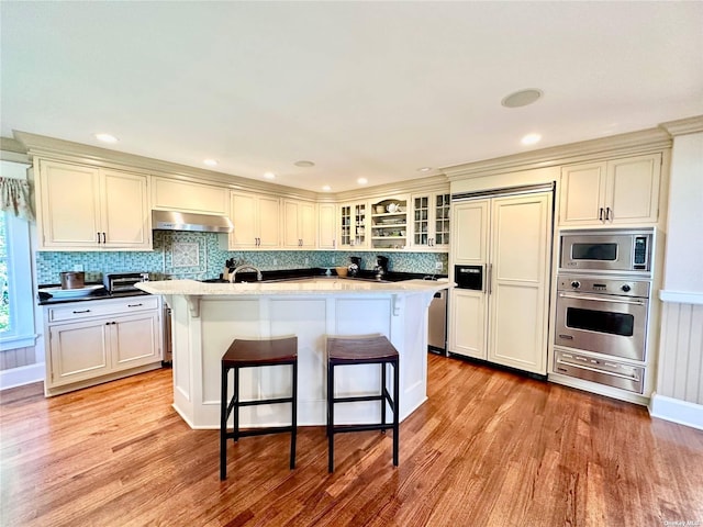 kitchen with built in appliances, light wood-type flooring, a breakfast bar area, and an island with sink