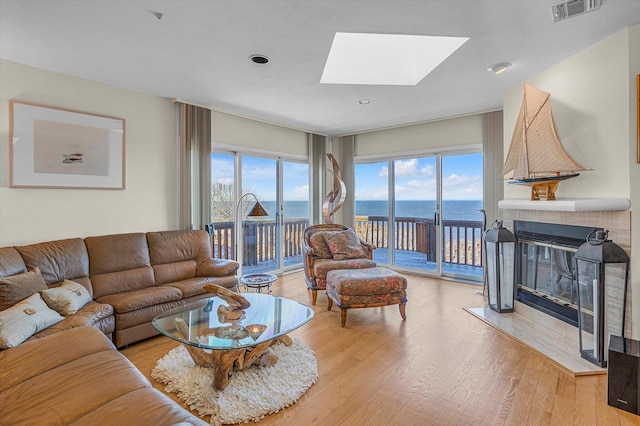 living room with a tiled fireplace, light hardwood / wood-style floors, a skylight, and a water view