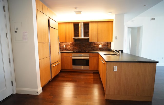 kitchen with sink, tasteful backsplash, stainless steel oven, dark hardwood / wood-style flooring, and wall chimney range hood