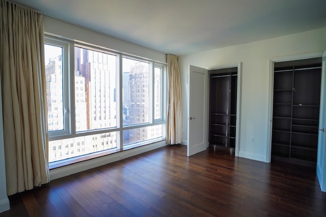 unfurnished bedroom with dark wood-type flooring and multiple closets