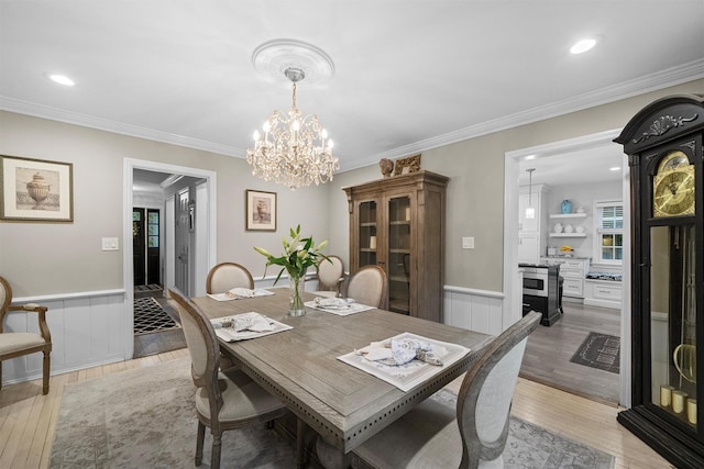 dining area with light hardwood / wood-style floors, ornamental molding, and a notable chandelier