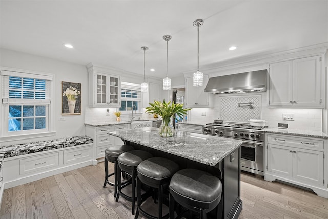 kitchen with high end stove, tasteful backsplash, wall chimney range hood, white cabinets, and a center island