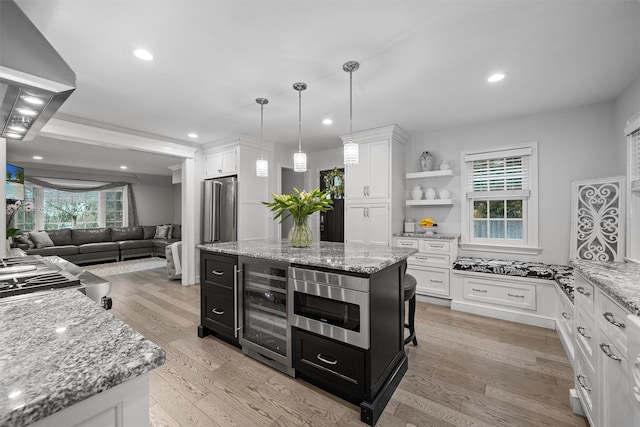 kitchen with white cabinets, a kitchen island, wine cooler, hanging light fixtures, and stainless steel microwave