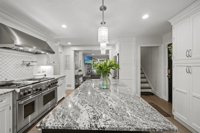 kitchen with double oven range, wall chimney range hood, white cabinetry, and a kitchen island