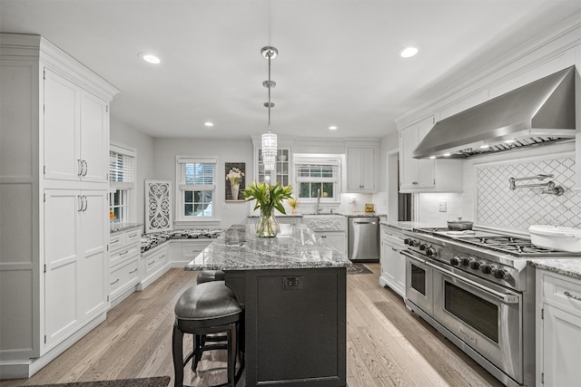 kitchen featuring light stone countertops, appliances with stainless steel finishes, wall chimney exhaust hood, a kitchen island, and light hardwood / wood-style floors