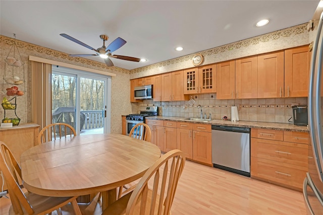 kitchen featuring sink, light wood-type flooring, ceiling fan, stainless steel appliances, and light stone countertops