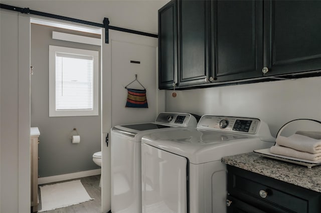 laundry area featuring washing machine and dryer, cabinets, a barn door, and light hardwood / wood-style flooring