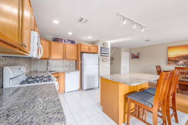 kitchen featuring a kitchen island, a breakfast bar, light stone counters, track lighting, and white appliances